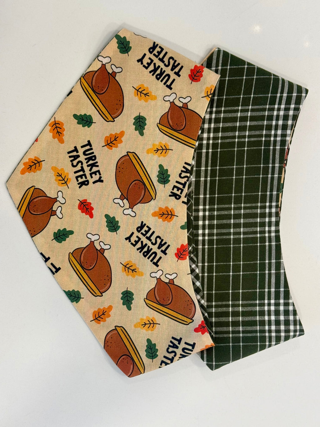 Turkey Taster bandana with roast turkey and autumn leaf print beside its dark green plaid reverse